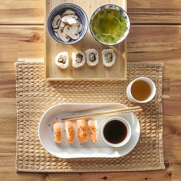 Top view of sushi, drinks, and plates on wooden table. Plate holds sushi with chopsticks and soy sauce.