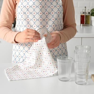 Person wearing an apron with a loop for hanging, holding a glass. Stacked glasses on a counter.