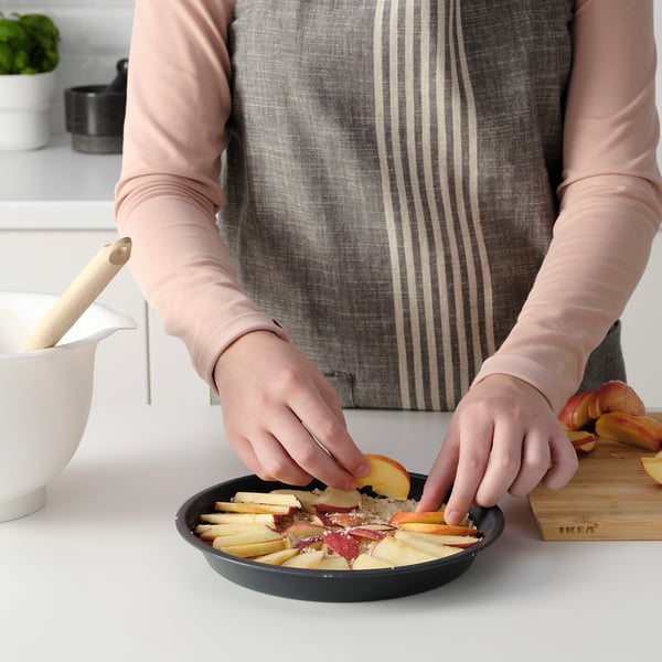 Person prepares apple slices in a black pie dish with a non-stick coating for baking.