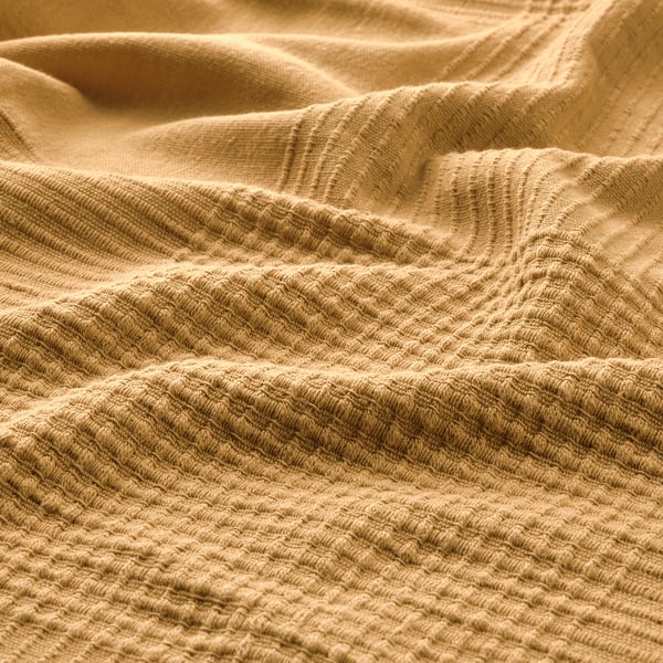 Soft, textured golden bedspread, crafted with intricate weave, providing warmth and comfort.