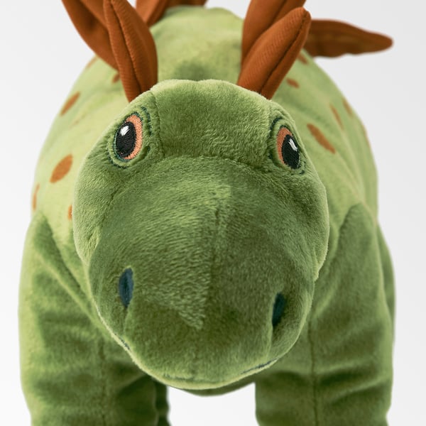 Green stuffed dinosaur toy with brown spots and horns, soft and plush, standing upright.