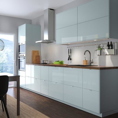 Modern kitchen with grey-blue cabinets, stainless sink, wooden counter. Tall units with built-ins.