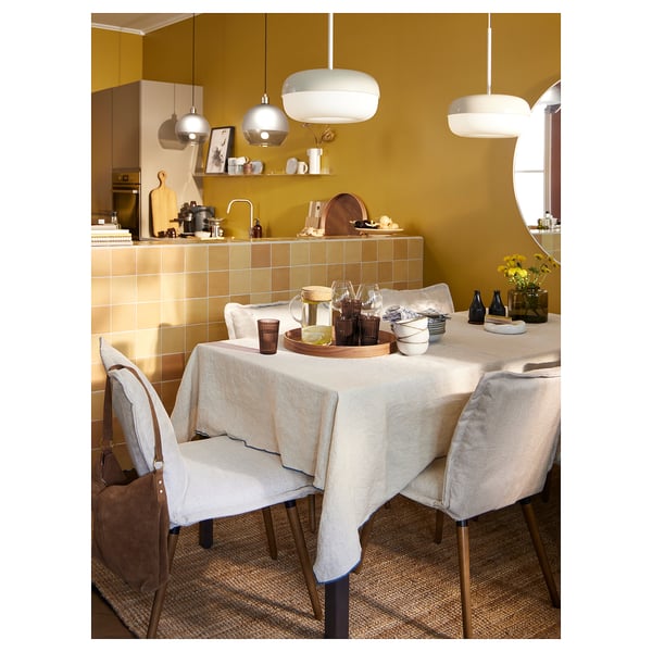 Modern dining area with yellow walls, tiled backsplash, and a table set for four. Pendant lights above, chair with bag.