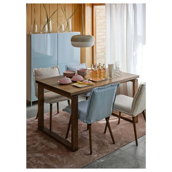 Modern dining setup with KLINTEN chairs in blue and beige, dark wood table, stylish pendant light, and glassware on table.