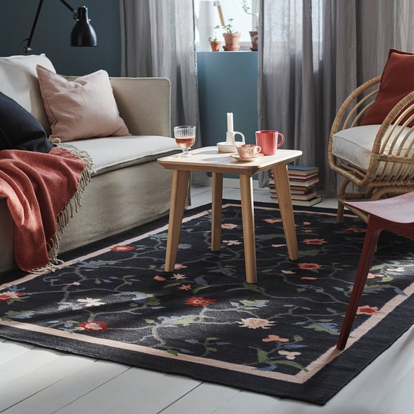 Living room with grey sofa, wooden side table, and black rug with floral design.