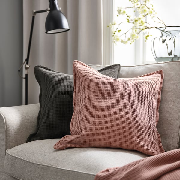 Living room: grey sofa, pink pillows, lamp, flowers, curtains, natural light.