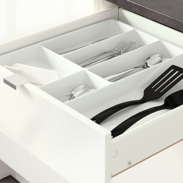 White kitchen drawer with dividers, storing cutlery and black spatulas.