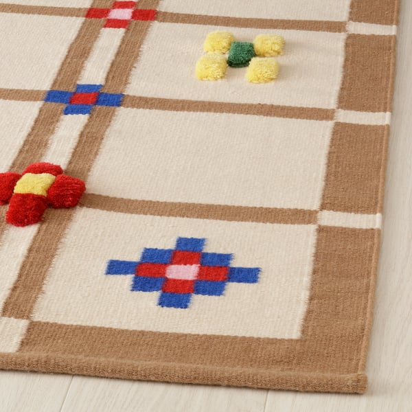 Handwoven rug with intricate patterns in neutral and colourful squares, featuring plush pom-poms.