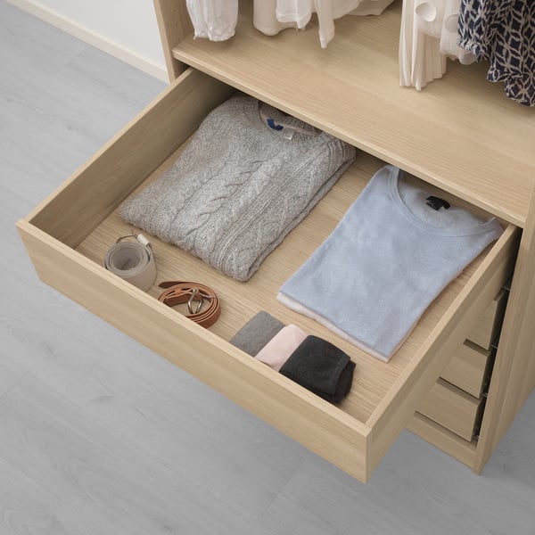 Open wooden drawer showing folded sweater, shirt, socks, and accessories, demonstrating organised storage in a wardrobe.