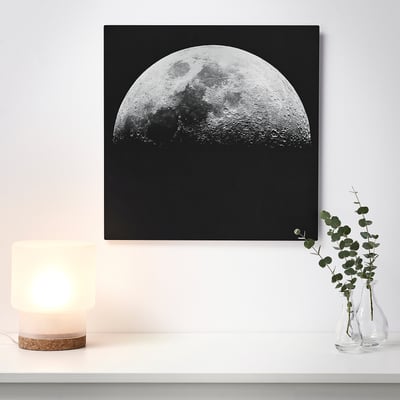 A wall art of a half moon on a black background, illuminated by a nearby lamp, giving a 3d effect.