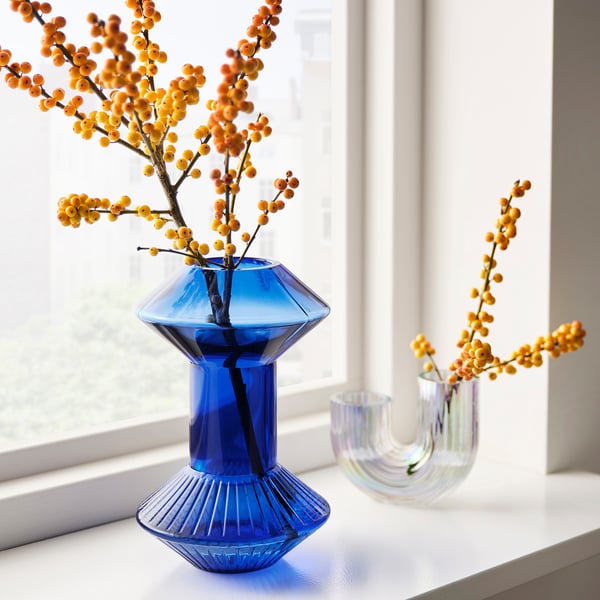 KRYPOXBÄR: blue, geometric glass vase on window sill, with orange berry branches. Smaller clear glass vase nearby.