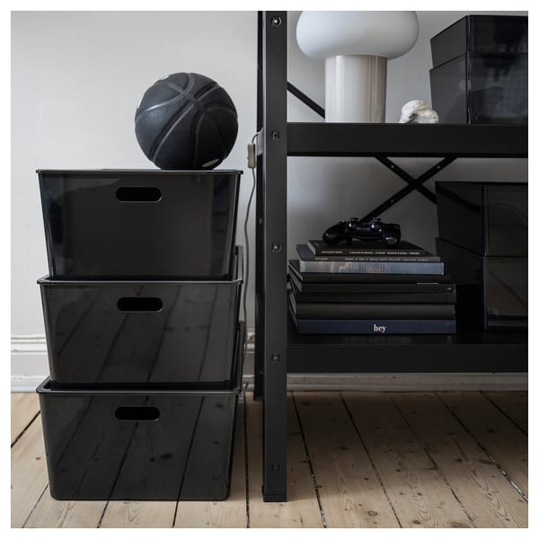 Stacked KUGGIS boxes with handles, basketball on top, shelf with books and lamp behind.