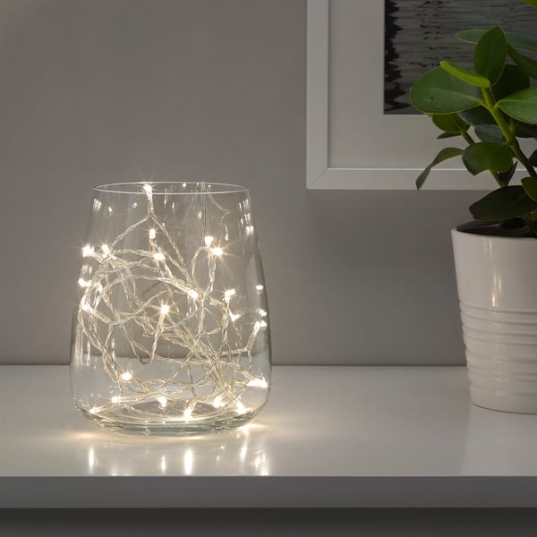 Clear glass vase with warm white led lights casting a festive glow on a white shelf.