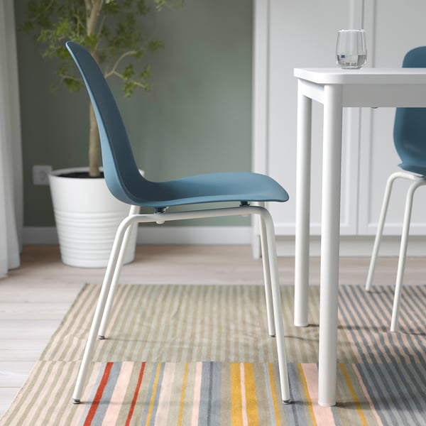 Blue chair with white legs on striped rug near white table.