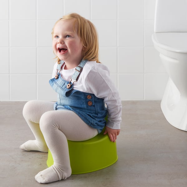 A toddler sitting on a green LILLA pottyrainer, designed for toilet training with non-slip base.