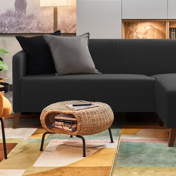 Modern dark grey fabric sectional sofa with grey pillows on a multicoloured rug.