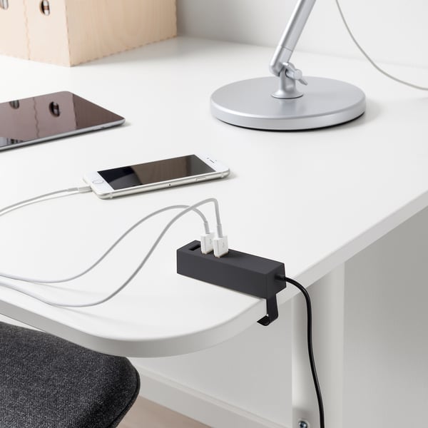 A sleek black usb charger sits on a white desk, holding three connected white cables that power a smartphone and other devices.