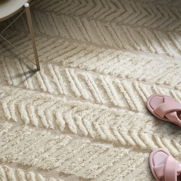 Beige, handcrafted wool rug with geometric fur rows beside pink sandals.