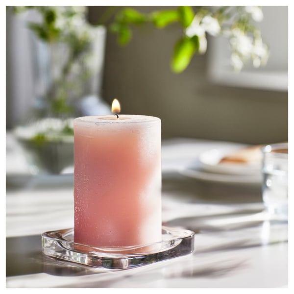 A pink LUGNARE scented candle on a clear glass holder, emitting a warm glow with a romantic atmosphere.