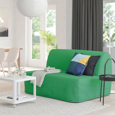 Modern living room with green lycksele sofa, natural light, colourful pillow, coffee table with plant, and black side table.