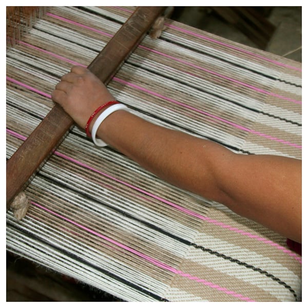 Image shows hands weaving colourful fabric on a loom.
