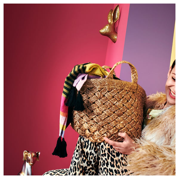 A person in a leopard print dress, holding a woven brown basket with colourful tassels.