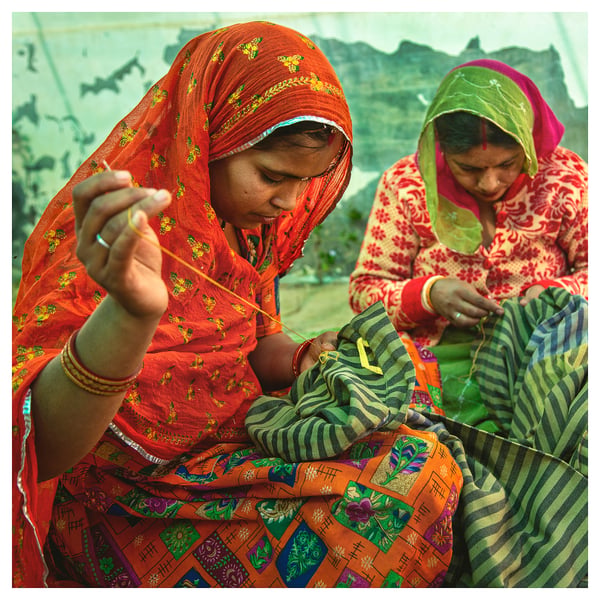 Two people sewing in colourful traditional attire.