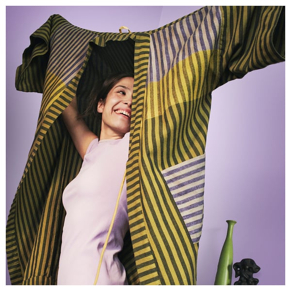 Person in striped yellow-green bathrobe smiling, holding cloth over head.