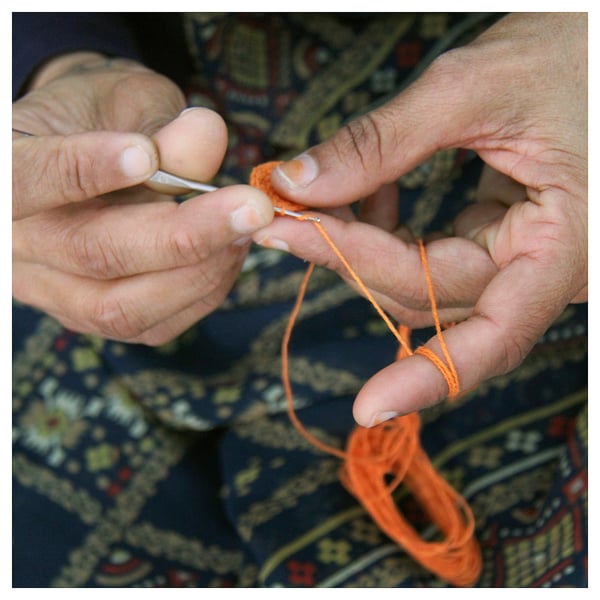 Person crocheting orange yarn. Hands focused on crafting intricate design.