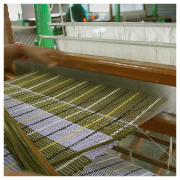 Loom weaving colourful fabric, creating MÄVINN rug. Vibrant stripes on cotton, intricate design.