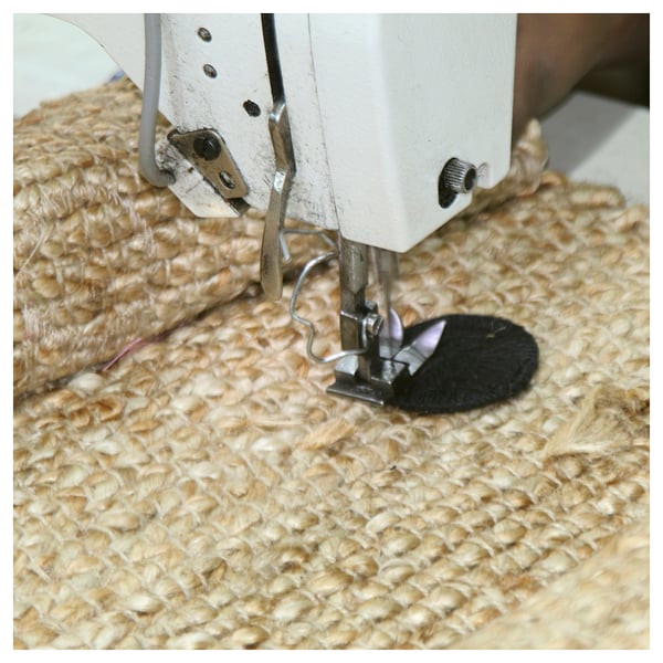 Sewing jute fabric on machine. White sewing machine, beige textured jute, black presser foot. Close-up view.