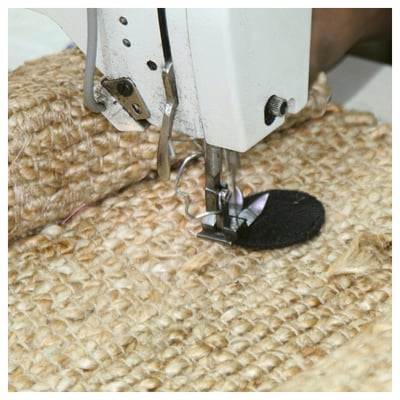 Sewing jute fabric on machine. White sewing machine, beige textured jute, black presser foot. Close-up view.