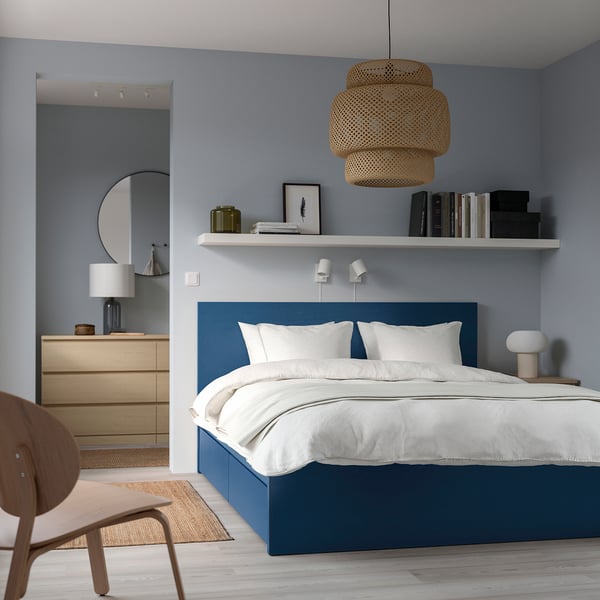 Minimalist bedroom with blue MALM bed, white shelf, wooden dresser, chair, and rug.