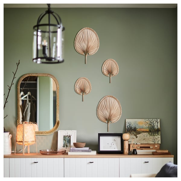 Green wall with white cabinet, mirror, hanging fans, lamp, art, books, and vases.