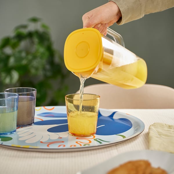 A clear plastic jug with a yellow lid pours lemonade into a glass. Its a stylish way to keep drinks chilled for longer using the frozen insert.