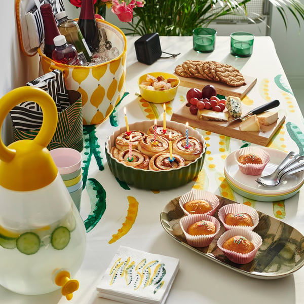 Colourful party table with NÄBBFISK yellow pitcher, desserts, cheese, drinks, and decorative items.
