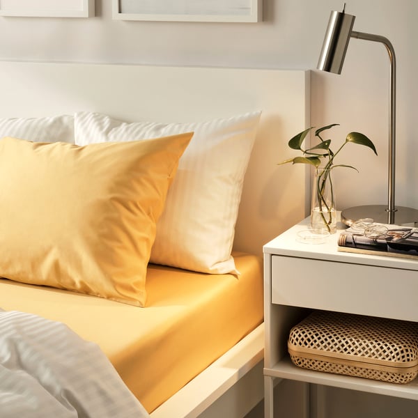 Yellow bed in cosy, minimalist bedroom with plant and books.