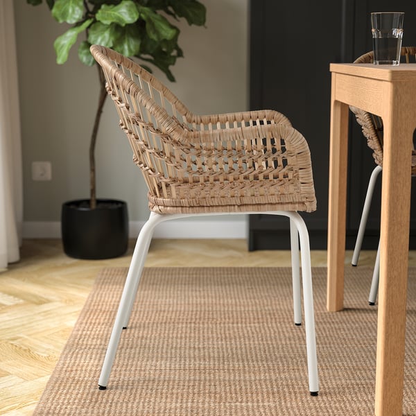 Woven rattan chair with white legs on a rug beside a wooden table.