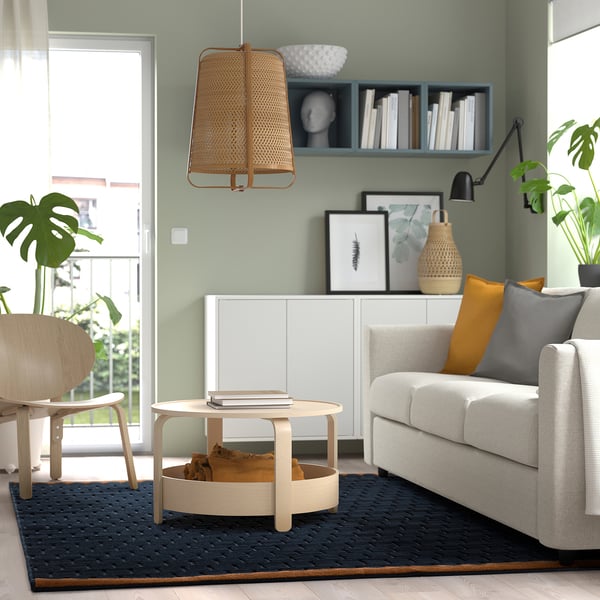 Modern living room with grey sofa, wooden coffee table, and blue rug. Light wood floors.