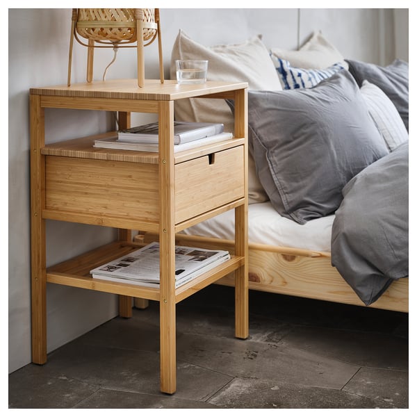 Light wooden bedside table with drawer, two shelves. Stores books, magazines, and a glass. Drawer accessible from both sides.
