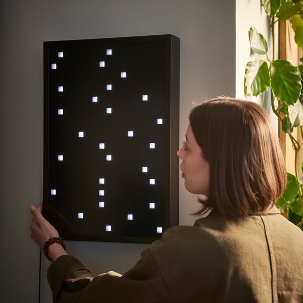 A person interacts with a black, rectangular OBEGRÄNSAD led wall lamp featuring a grid of illuminated squares.