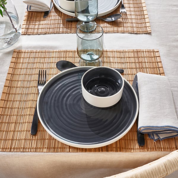 Table setting with grey ceramic bowl on plate, glass, fork, spoon, and napkin.