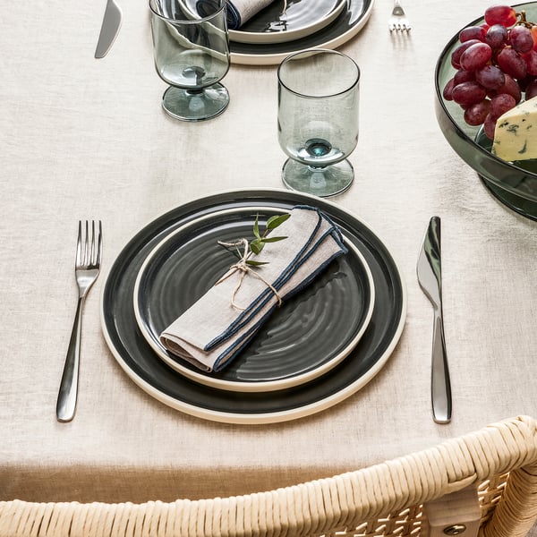 Grey table setting with folded napkins, greenery, silverware, glasses, and fruit & cheese.
