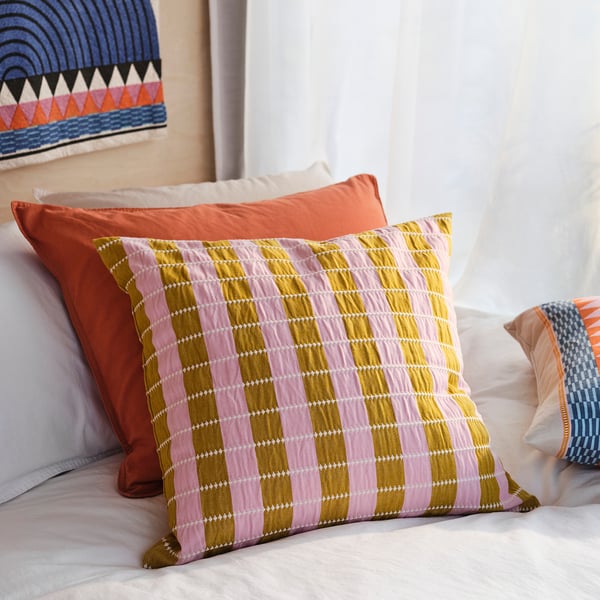 A cosy bed with colourful pillows. A patterned pillow has pink, yellow, and white stripes.