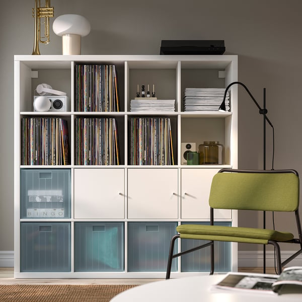 Modern living room with white bookcase, vinyl records, and home decor. Green chair and lamp nearby, featuring organised storage.