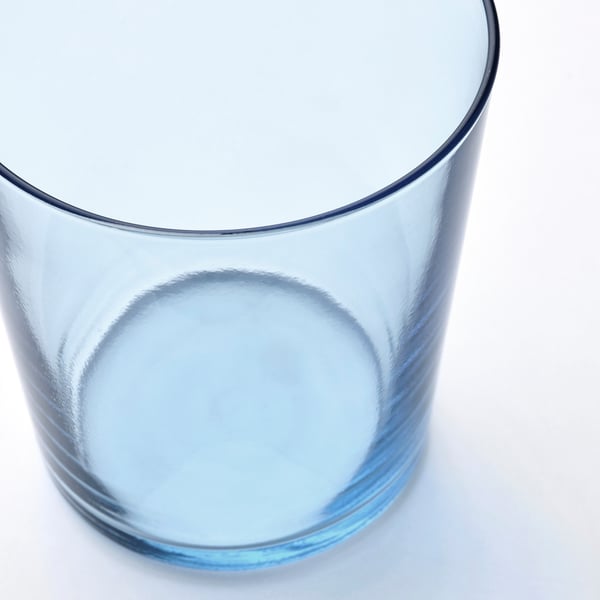 A clear blue glass cup on a white surface, reflecting light, showcasing its smooth texture and seamless design.