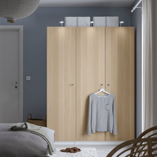 Minimalist bedroom with light wood PAX wardrobe, striped shirt, wicker basket, and white rug.