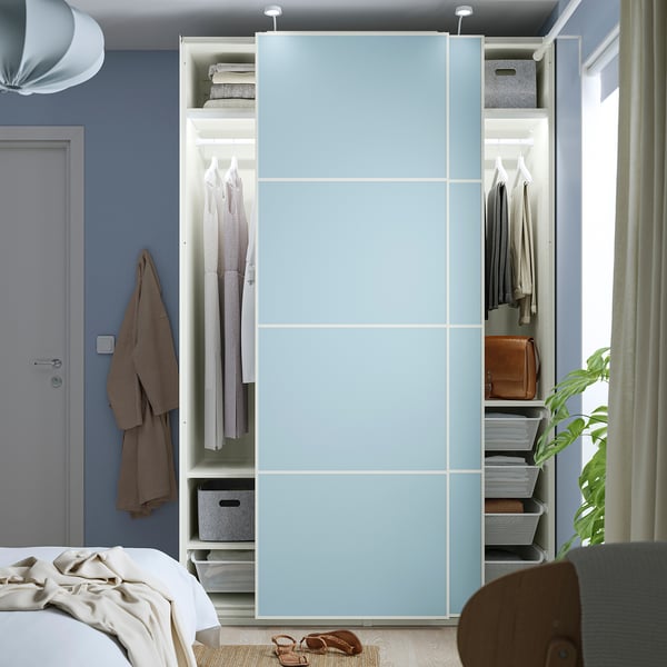 A modern bedroom a blue PAX wardrobe with sliding doors, revealing organised clothes and accessories inside.