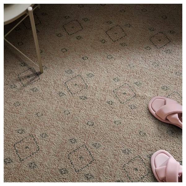 A beige wool rug with diamond patterns. A pair of pink sandals is on it.