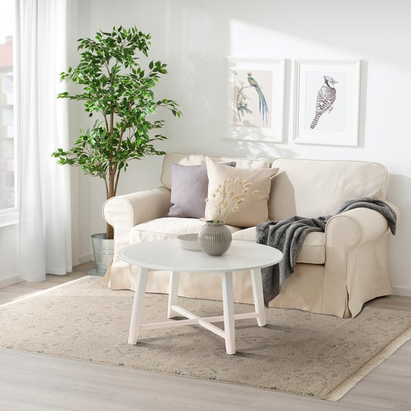 Neutral living room with beige sofa, white coffee table, and PENSELRÅG rug. Decorated with art, pillows, and plants.